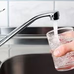 Man filling glass of water from kitchen sink