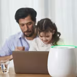 A father and his daughter sit at a table with a laptop, while HomePure Zayn ensures safe and clean indoor air
