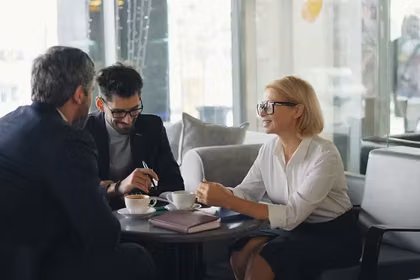 Woman mentoring two men in business leadership over coffee